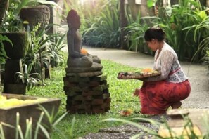 A person carrying a tray with food items, surrounded by greenery and a stone structure. - Gusde House and Villa Bali (Bali)