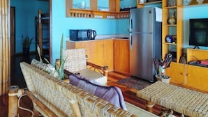 A kitchen with wooden cabinets, a refrigerator, a microwave, and a dining area with a woven bench. - Casa Nena Hotel and Resort Iloilo (Miagao)