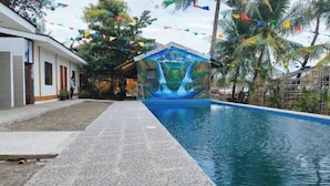 A swimming pool with a mural of a waterfall, surrounded by palm trees and colorful flags. - Casa Nena Hotel and Resort Iloilo (Miagao)