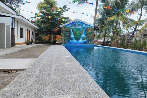 Una piscina con un murale raffigurante una cascata, circondata da palme e bandierine colorate.
