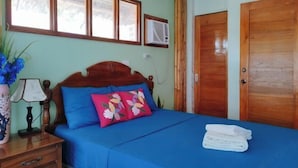 A bedroom with a wooden bed, blue bedding, a nightstand with a lamp, and a window with blinds. - Casa Nena Hotel and Resort Iloilo (Miagao)