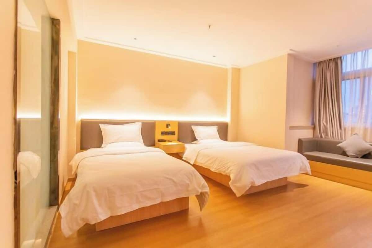 Une chambre d’hôtel avec deux lits, un canapé, une table de chevet et une grande fenêtre avec des rideaux.