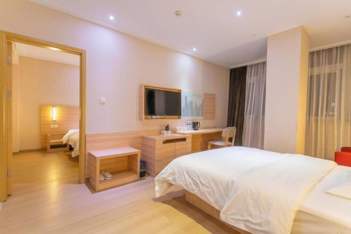 Une chambre d’hôtel avec un lit, un bureau, une chaise, un miroir, une télévision et une fenêtre avec des rideaux.