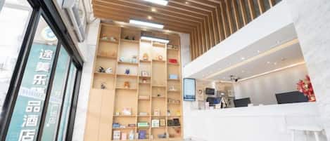 A hotel reception area with a modern design, featuring a reception desk, a wall-mounted display, and a series of shelves with various items.