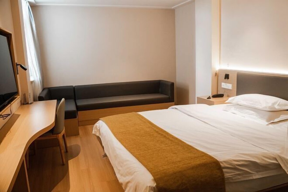 A hotel room with a bed, a desk, a chair, and a bench.