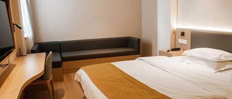 A hotel room with a bed, a desk, a chair, and a bench.