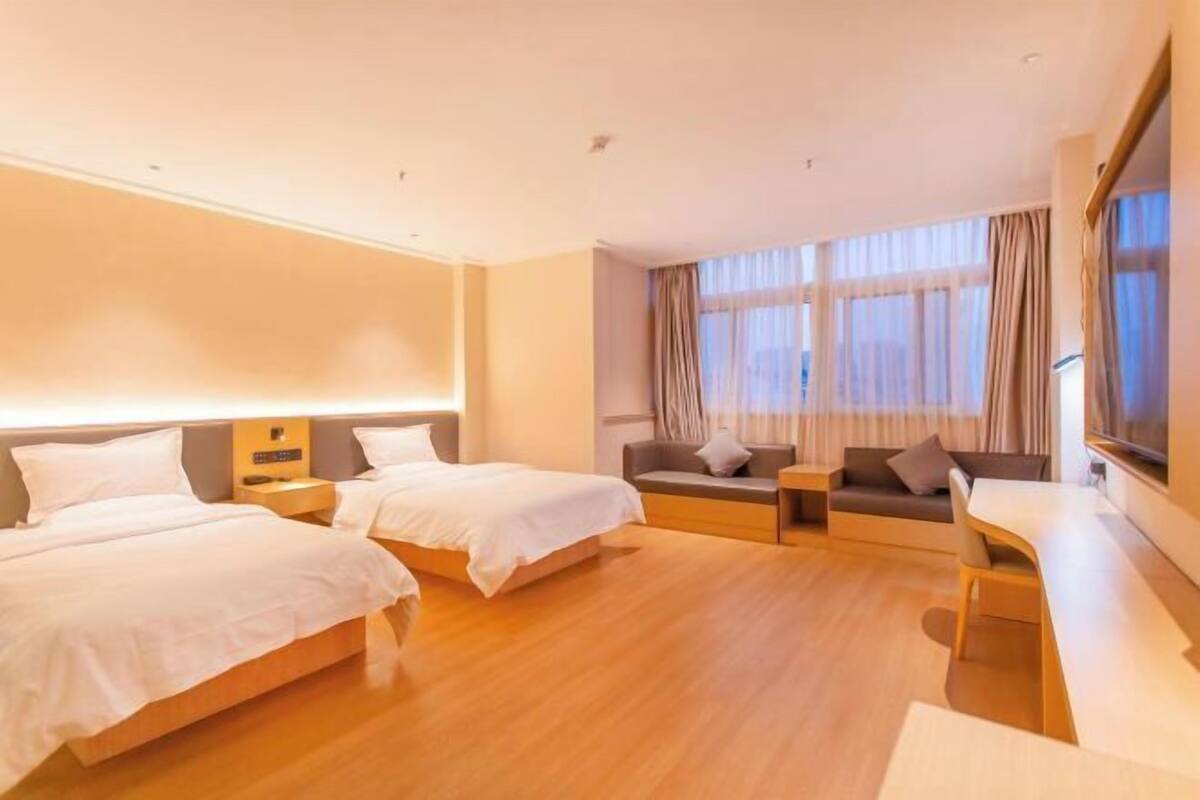 Une chambre d’hôtel avec deux lits, un canapé, une télévision et une grande fenêtre avec des rideaux.