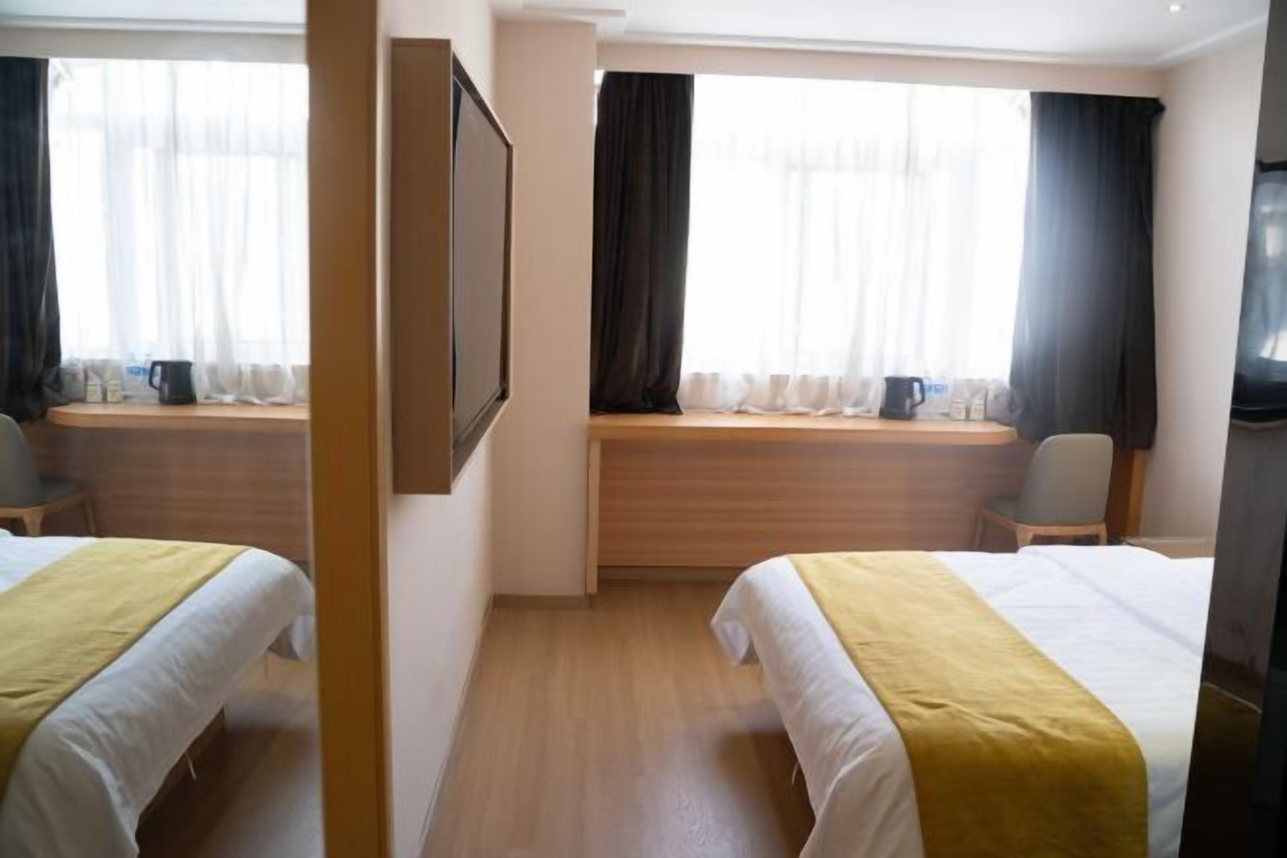 A hotel room with two beds, a wooden bench, a television, and a window with curtains.