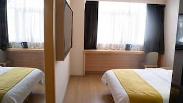 A hotel room with two beds, a wooden bench, a television, and a window with curtains.