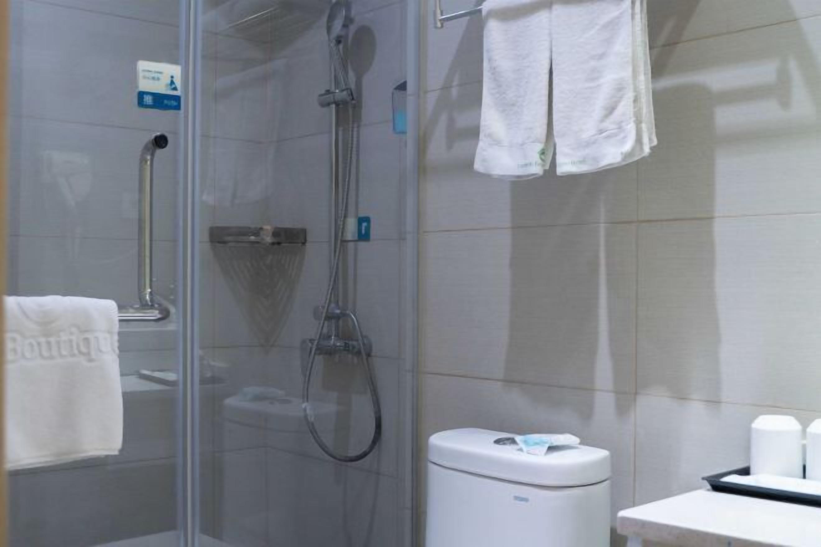 Un baño con cabina de ducha de vidrio, un inodoro blanco y un perchero con una toalla blanca.