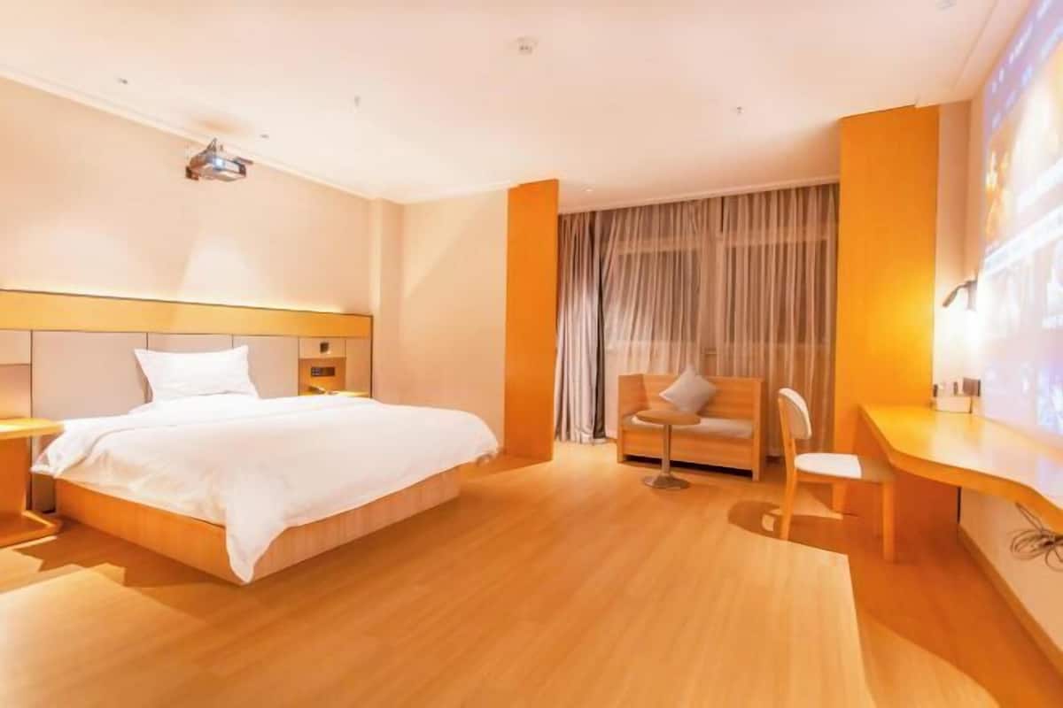 Une chambre d’hôtel moderne avec un grand lit, un bureau, une chaise et une fenêtre recouverte de rideaux.
