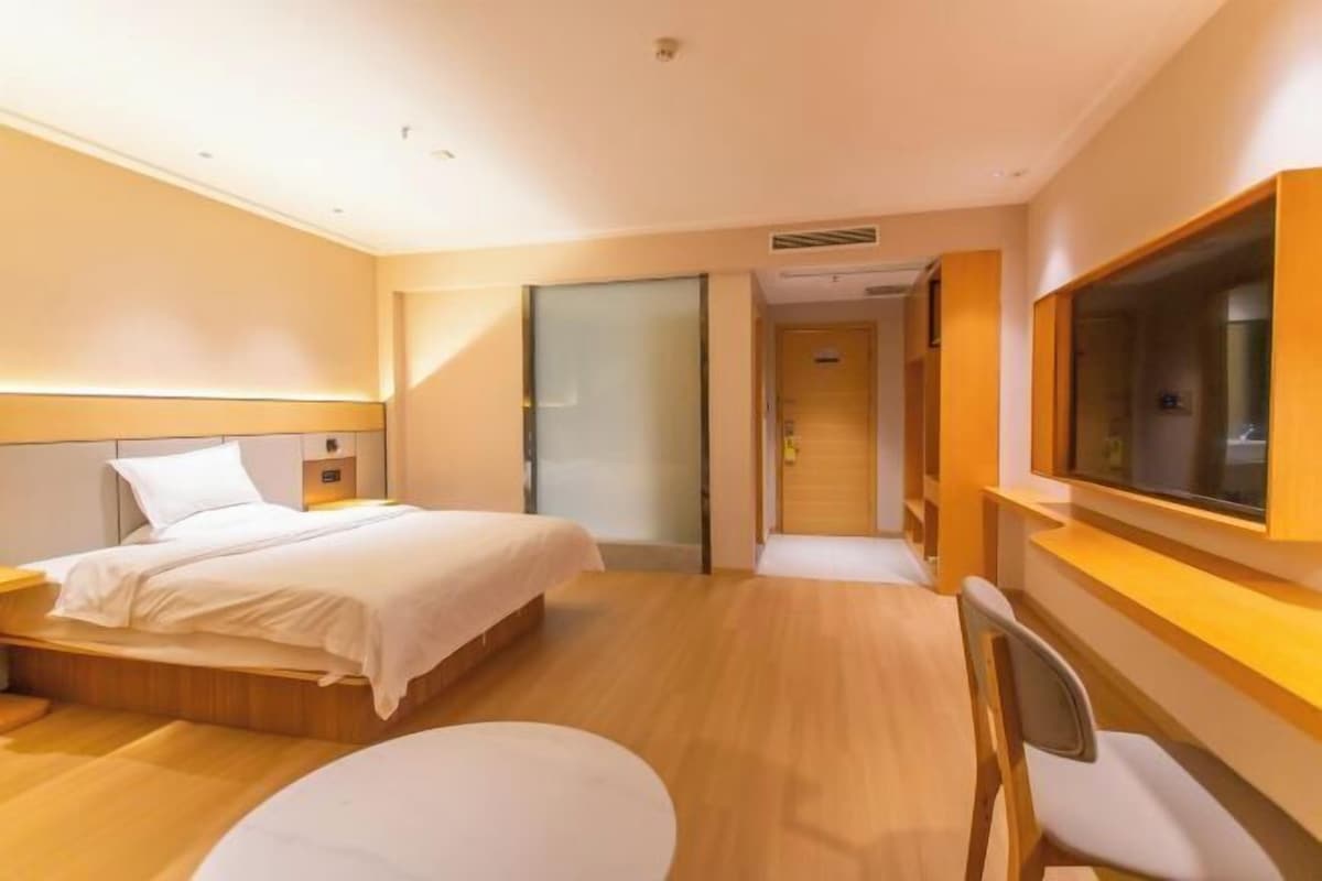 A hotel room with a bed, a desk, a chair, a TV, and a door leading to another room.