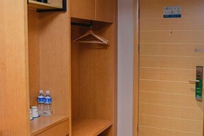 Une armoire en bois avec une tringle pour suspendre les vêtements et une étagère où sont posées des bouteilles d’eau.