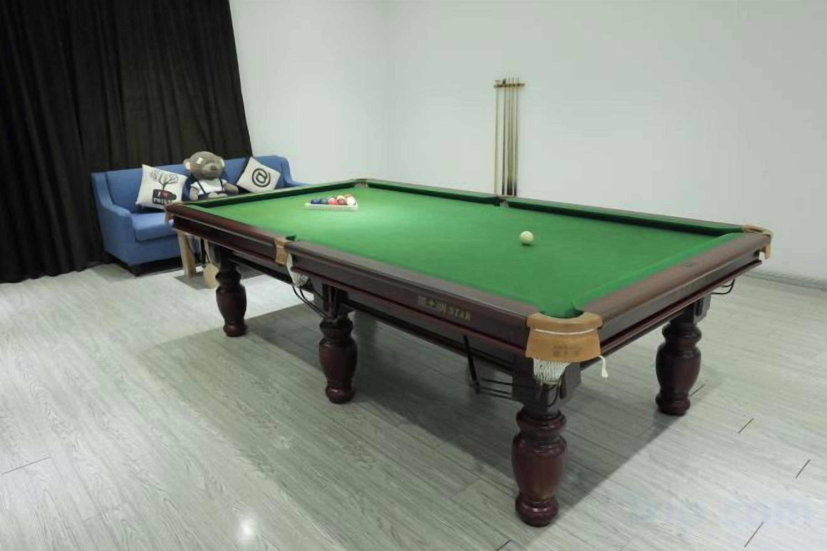 Una mesa de billar con superficie de fieltro verde, un sofá azul con cojines y una cortina negra al fondo.