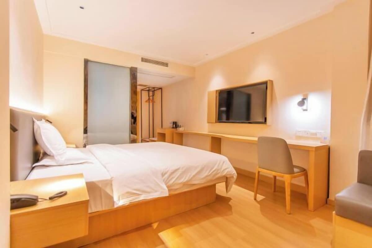 A hotel room with a bed, a desk, a chair, a TV, and a wardrobe.