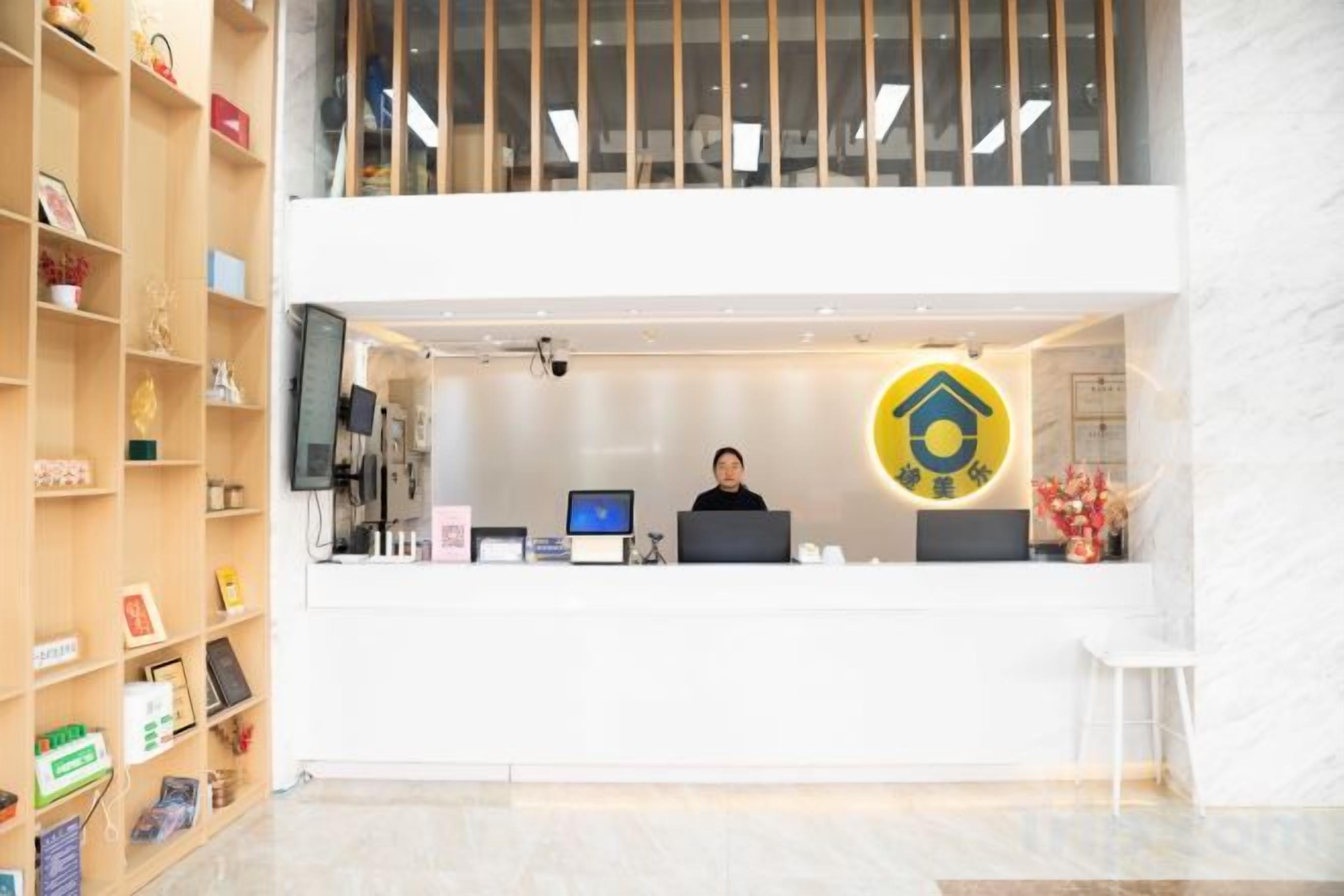 A reception desk with a computer, a monitor, and a person seated behind it. There is a large circular logo above the desk.