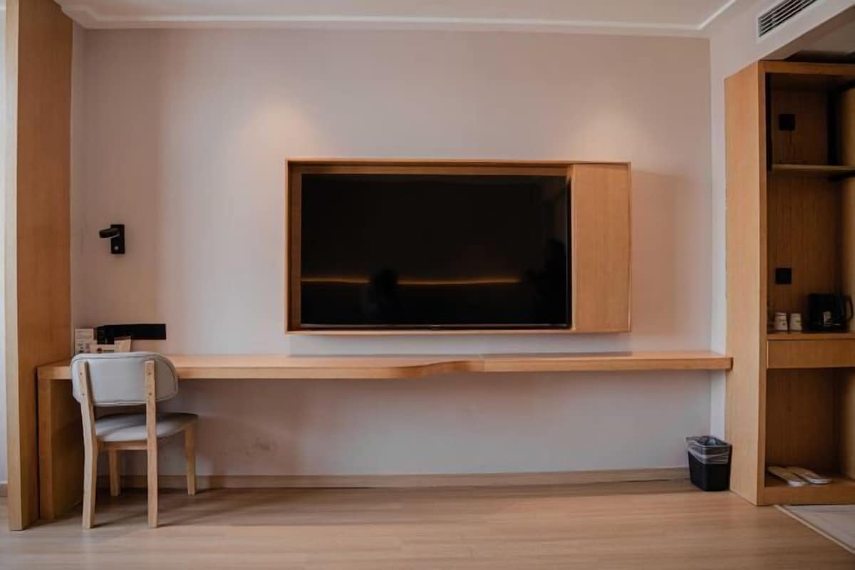 A minimalist room with a wooden desk, a chair, and a television mounted on the wall.