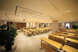 Une salle de conférence avec des rangées de tables et de chaises, une grande plante et un écran de projection.