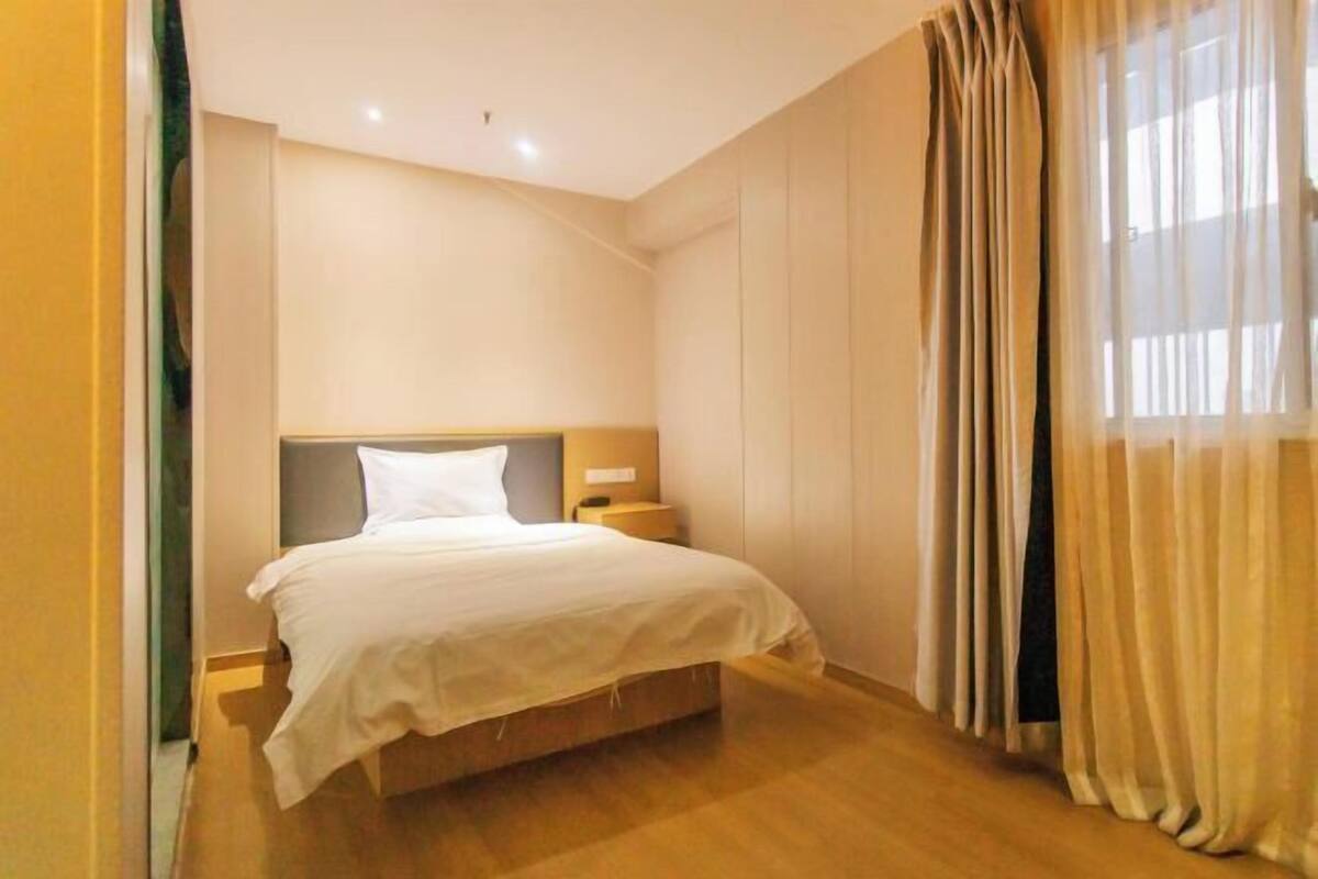 Une chambre d’hôtel avec un lit, des tables de chevet, une fenêtre avec des rideaux et un plancher en bois.