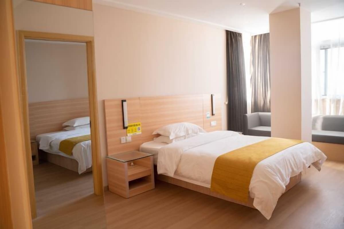 A hotel room with a large bed, a bedside table, a chair, and a view of the outside.