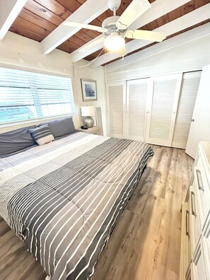 Un dormitorio con cama, ventilador de techo, ventana con persianas y puerta con contraventanas.