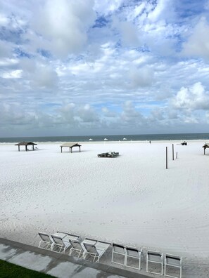 A beach with white sand, a row of empty beach chairs, and a few beach umbrellas.