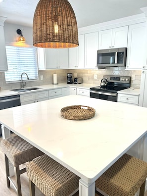 A modern kitchen with white cabinetry, a central island, a woven basket, and a hanging light fixture.