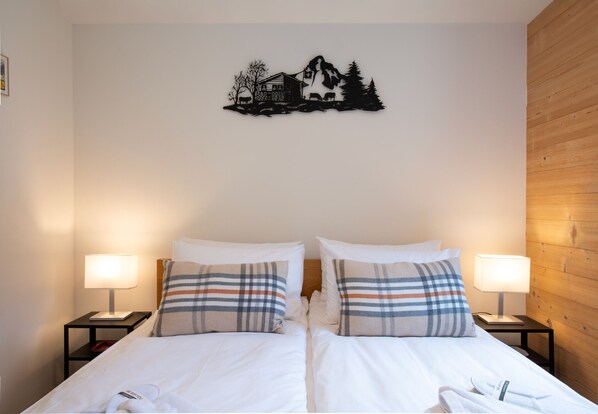Ein Doppelbett mit weißer Bettwäsche, zwei Nachttische mit Lampen und ein Wandbild mit einer Berglandschaft.