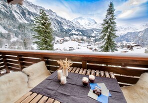 Eine Holzterrasse mit einem für zwei Personen gedeckten Tisch, Kerzen, einer Vase mit Trockenblumen und einer Schale Trauben.