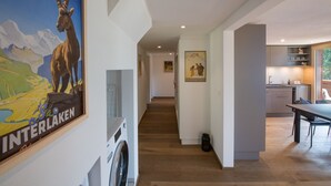 Un intérieur moderne avec un long couloir menant à une cuisine et à un espace repas. Une grande affiche représentant un paysage de montagne est visible sur le mur de gauche.