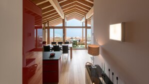 Interior moderno com teto alto, vigas de madeira, área de jantar com cadeiras e mesa, e vista através de amplas janelas.
