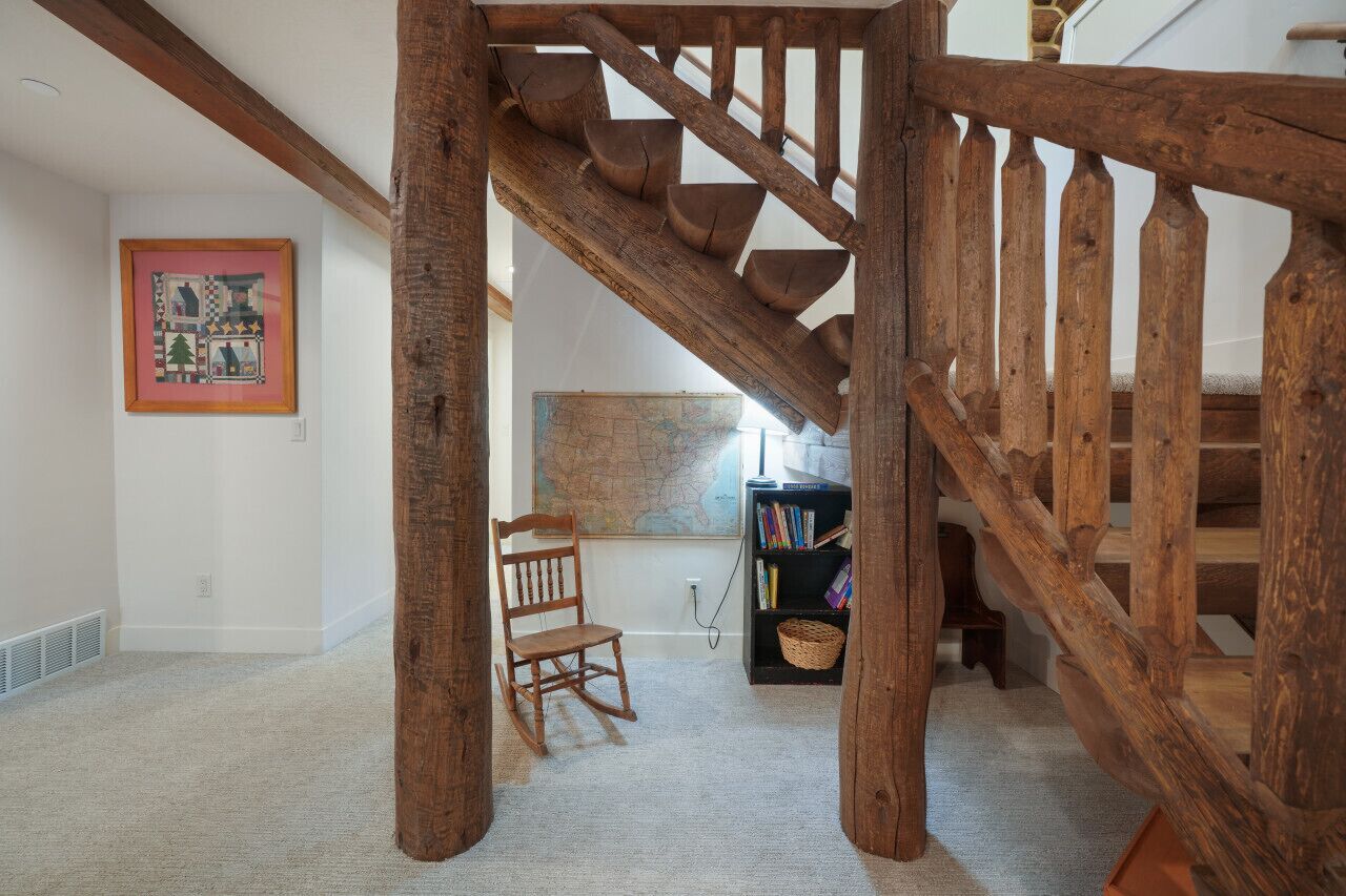 Eine Holztreppe mit rustikalem Design, ein Schaukelstuhl, ein Bücherregal und ein gerahmtes Bild an der Wand.