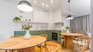 A modern kitchen with white cabinets, a wooden dining table, and a built-in oven. - Doki Oliwkowy by Grand Apartments (Gdansk)
