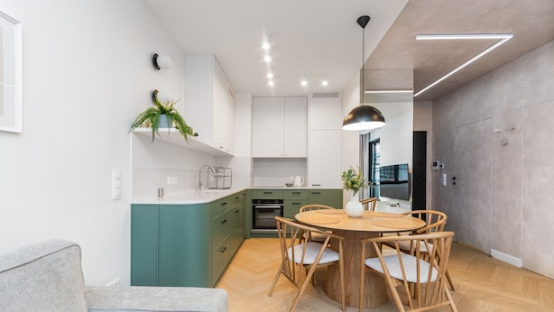 A modern kitchen with a dining area, green cabinets, wooden chairs, and a grey sofa. - Doki Oliwkowy by Grand Apartments (Gdansk)