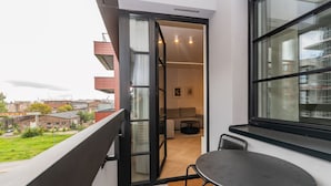 A balcony with a table and chairs, an open door leading to a room with a sofa and a coffee table, and a view of the surrounding buildings. - Doki Oliwkowy by Grand Apartments (Gdansk)