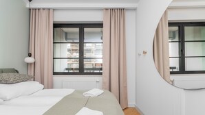 A bedroom with a bed, a window with curtains, a radiator, and a view of buildings outside. - Doki Oliwkowy by Grand Apartments (Gdansk)