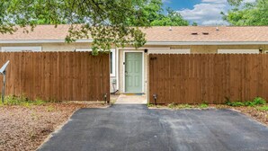 A single-story house with a green door, a wooden fence, and a paved driveway.