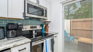 A kitchen with white cabinets, a stainless steel microwave, a stove, and a coffee maker.