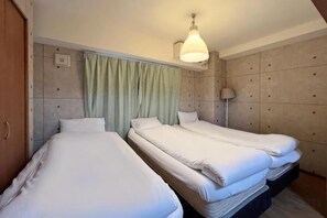 A hotel room with two single beds, a wooden wardrobe, a green curtain, a wall-mounted lamp, and a ceiling light.