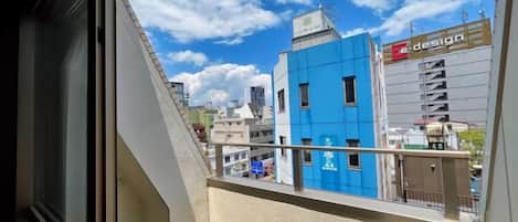 Vista da un balcone su un paesaggio urbano con edifici, tra cui un palazzo blu con un cartello che riporta la scritta 'design'.