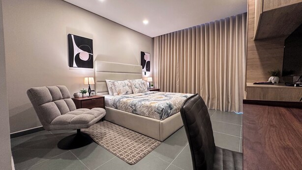 Un dormitorio moderno con cama, una silla, una mesita de noche y televisión.