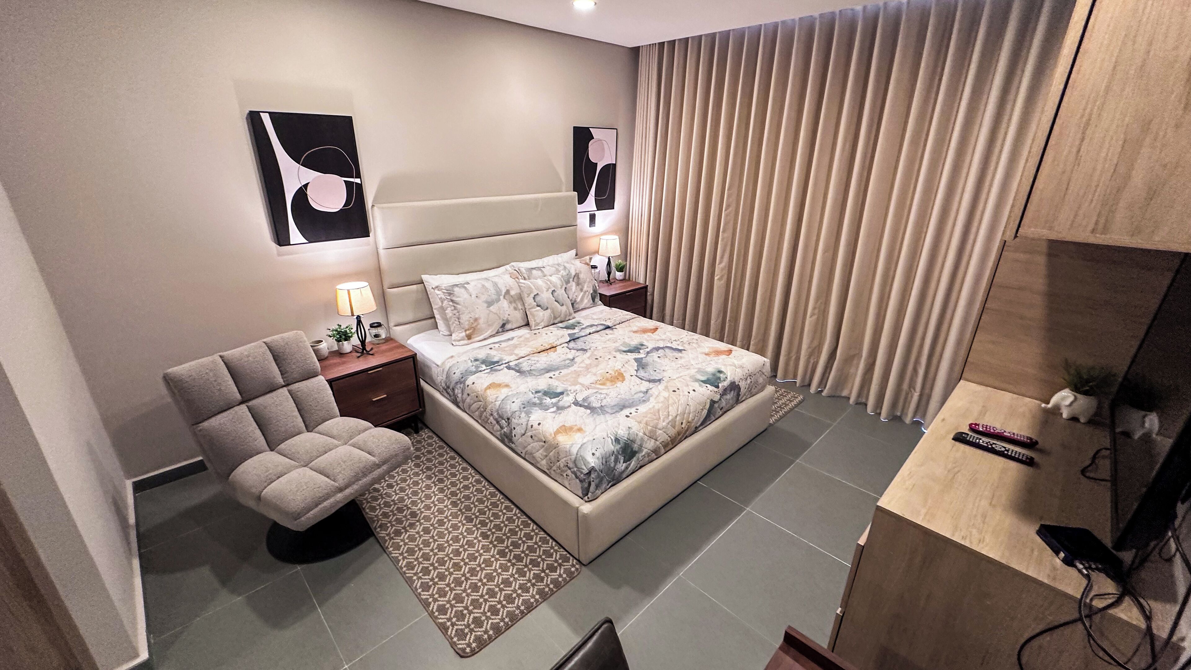 A modern bedroom with a bed, bedside tables, a chair, and a TV stand.