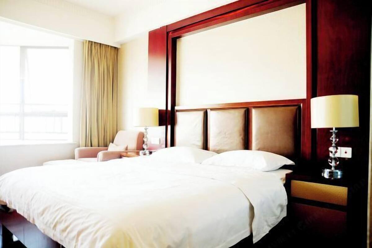 Ein Hotelzimmer mit einem großen Bett, einem Sessel, einem Nachttisch und einem Fenster mit Vorhängen.