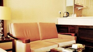 A hotel room with a sofa, a bedside table with a lamp, a small table with a remote control, and a kitchen area with a sink and cabinets. - Yupin Jing'an Ziyuan Apartment Hotel (Shanghai)