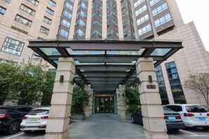 A multi-story building with a covered entrance, parking area, and a tall structure with many windows. - Yupin Jing'an Ziyuan Apartment Hotel (Shanghai)