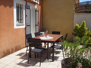 Een terras buiten met een houten tafel en stoelen, een fles wijn en een glas.