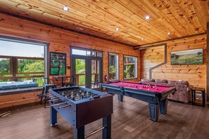 A wooden-floored room with a foosball table, pool table, and a sofa. - Spacious Cabin: Great views, convenient location, theater, game room, hot tub (Sevierville)