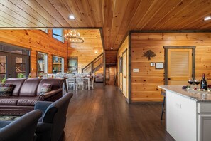 A spacious living area with a wooden ceiling, a brown leather sofa, a dining table with chairs, and a kitchen area with a countertop. - Spacious Cabin: Great views, convenient location, theater, game room, hot tub (Sevierville)