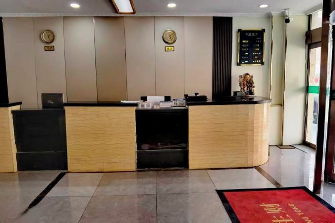 Un comptoir d’accueil avec un plan de travail en bois, un bureau noir à gauche et un tapis rouge menant à l’entrée.