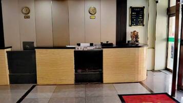 Un comptoir d’accueil avec un plan de travail en bois, un bureau noir à gauche et un tapis rouge menant à l’entrée.